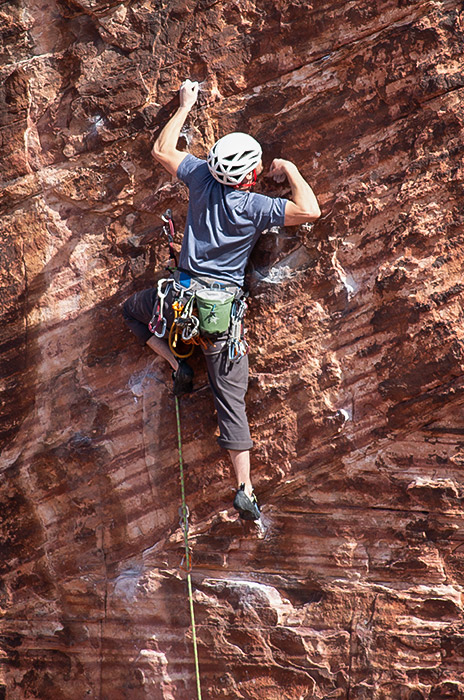 A close-up of a rock climber scaling a striated red wall.