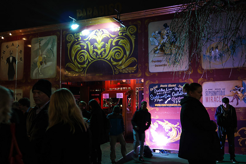 The Paradiso Spielgeltent in St. Andrew Square. The "tent" is actually a solid-fronted structure, maroon and purple in color with a gold design in the center right above the open doorway into the venue. Murals fill the Paradiso front, and a list of the acts appearing in the tent is painted on the right side of the door.